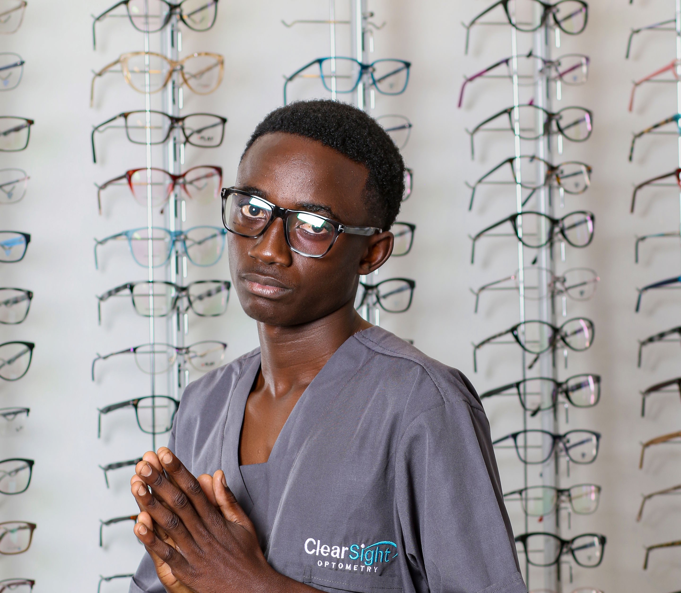 A happy Clearoptics customer wearing red-framed glasses in front of a wall of eyewear.